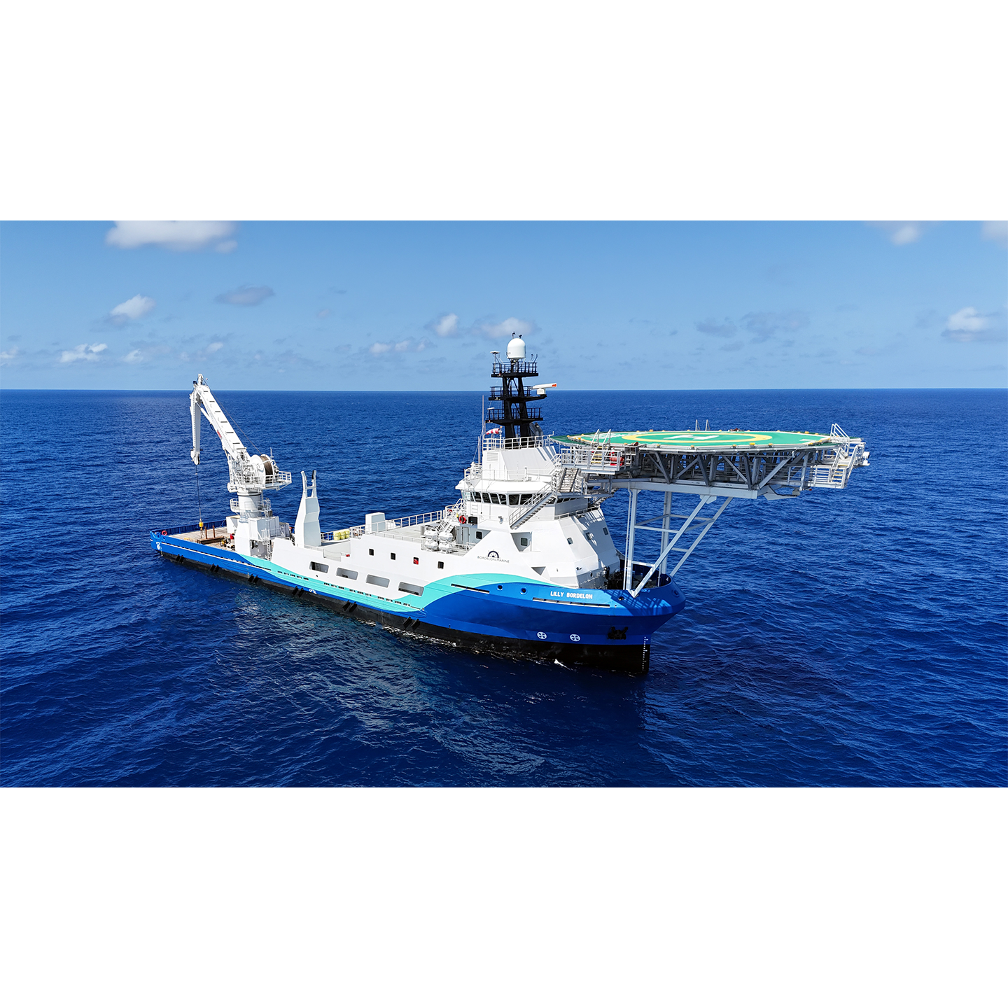 Offshore support vessel with a large helicopter deck and crane on blue ocean, white and blue hull.
